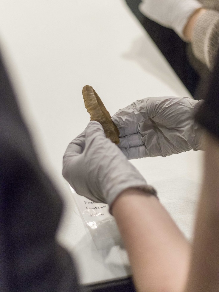 Close-up of hands holding neolithic stone tool in a lab setting. 