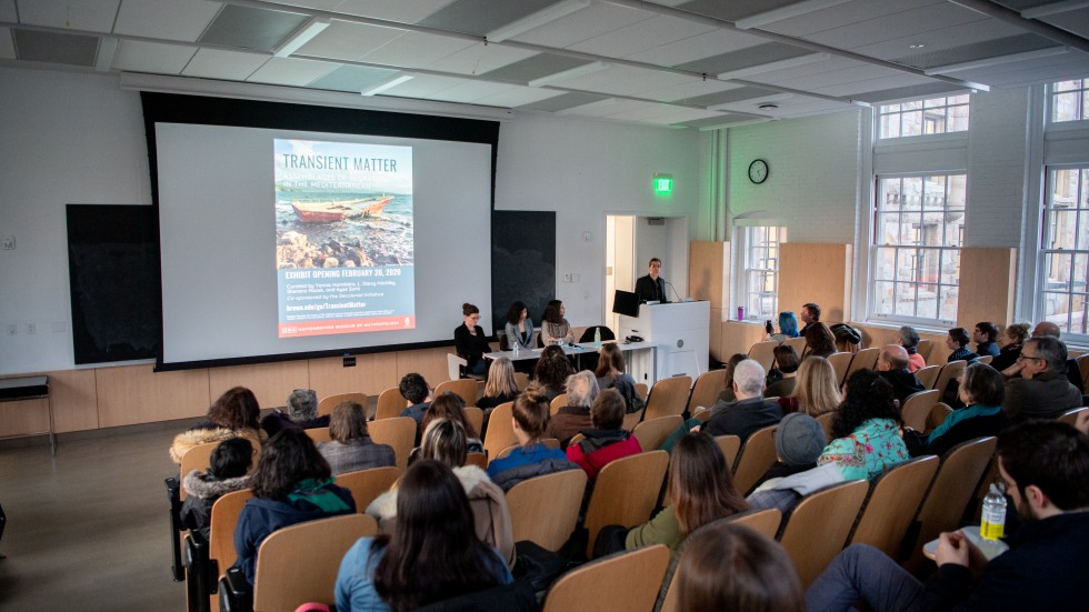 A crowd seated in a lecture hall listening to the curators' presentation.