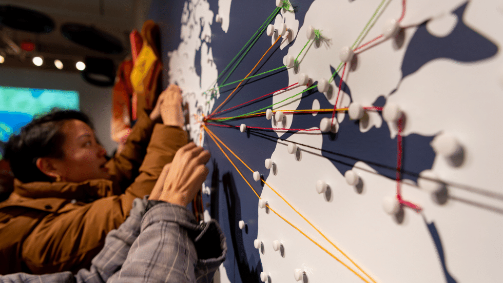 Visitors adding string to an interactive map wall in the Transient Matter exhibit.