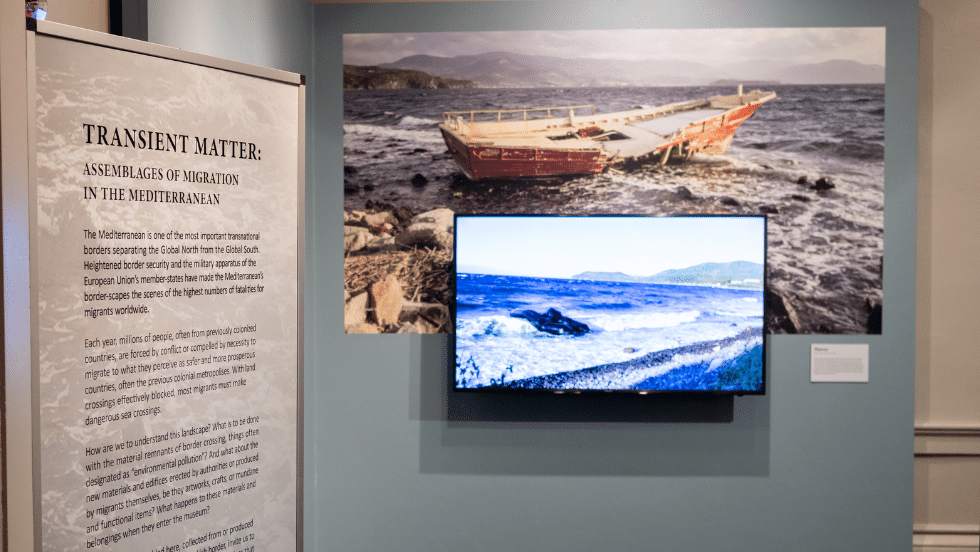 A photo, tv screen, and exhibit label on the wall of the Transient Matter exhibit. 