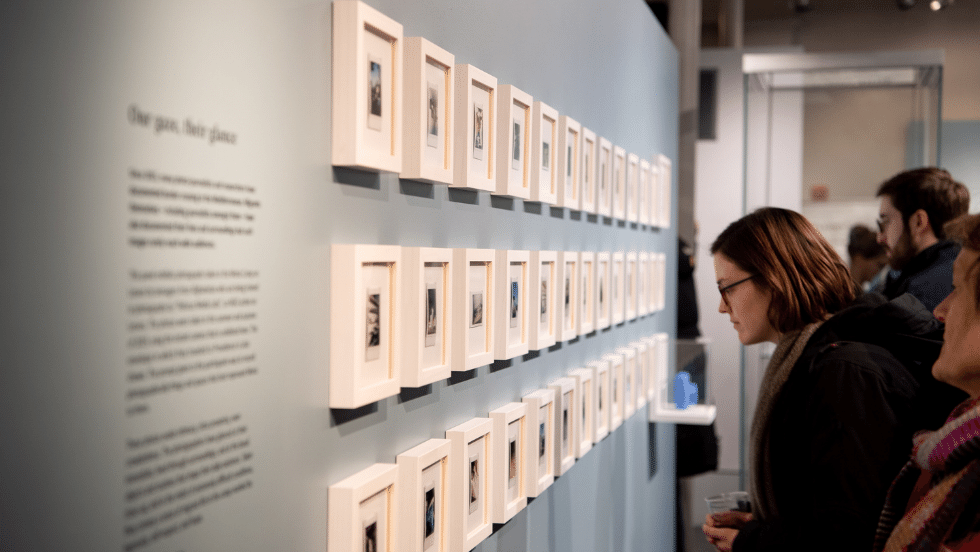 Visitors looking at a wall of framed polaroid photos in the exhibit. 