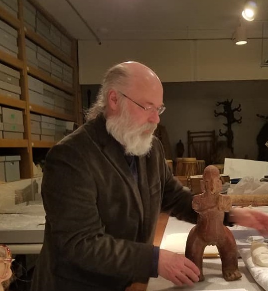 Photo of Curator Thierry Gentis in the collection storage, holding a carved wooden figure.