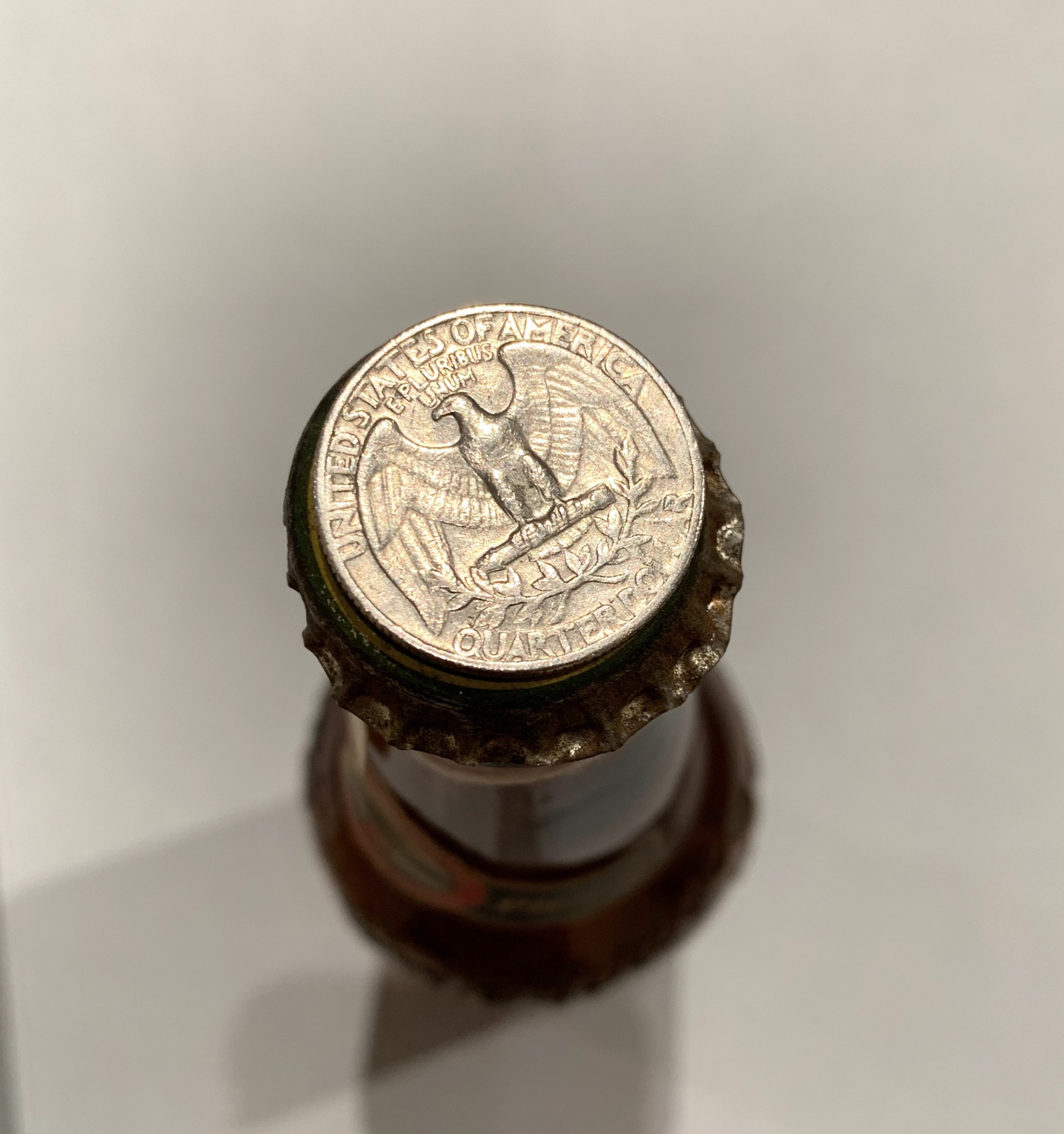Top-down photo of an antique beer bottle with a USA quarter on the bottle cap.