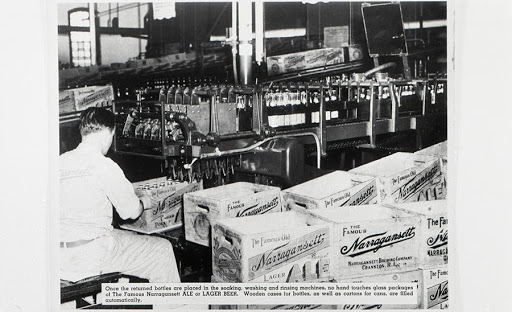 Black and white newspaper photo of Narraganset Brewing Company bottling plant, with one man, bottles, and crates pictured. 
