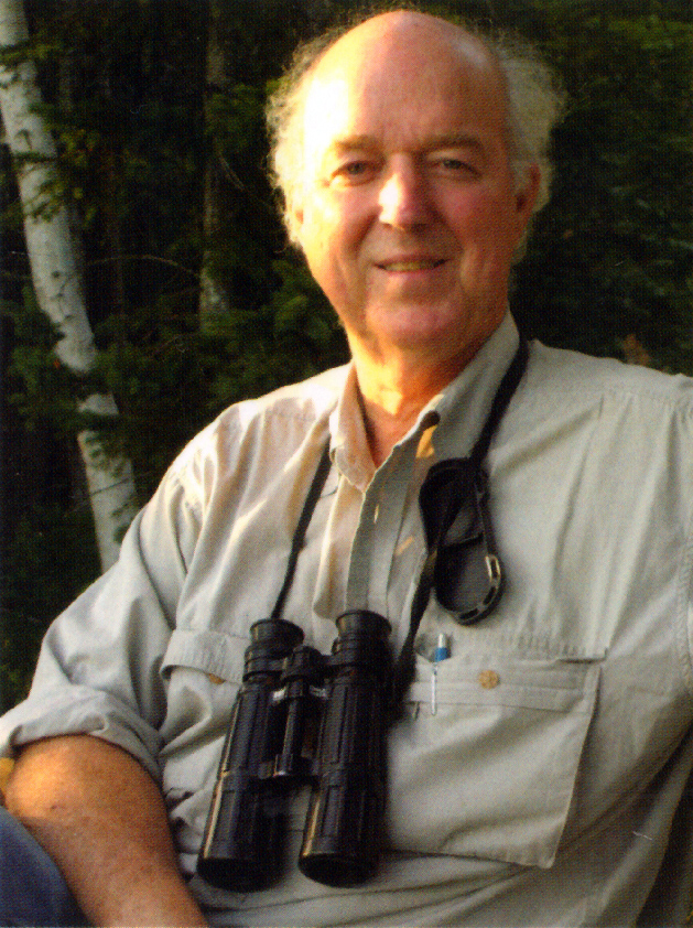 Photo of Shepard Krech III seated outside with binoculars hanging from his neck.