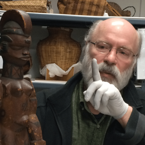 Candid photo of Thierry Gentis holding an African figure in the museum collection storage.
