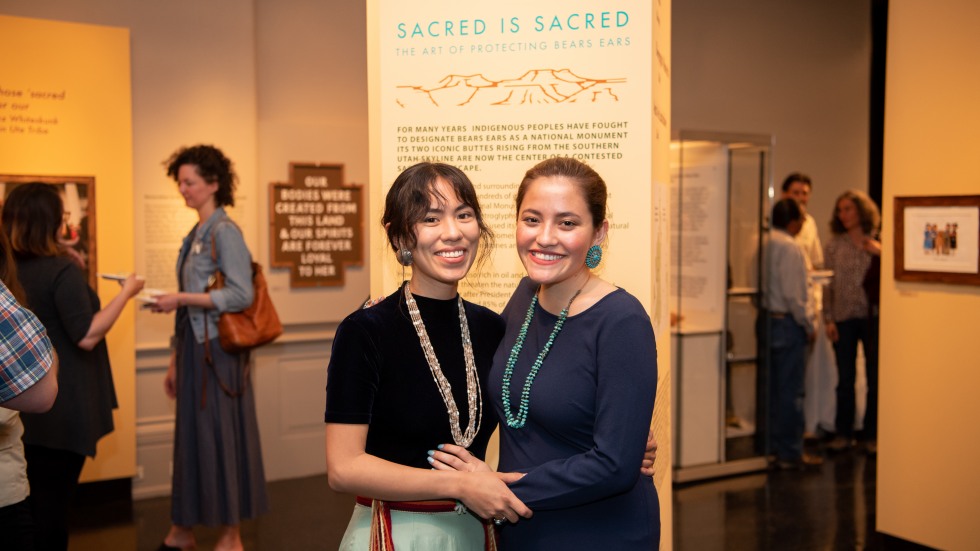 Two woman stand in front of newly installed "Sacred is Sacred" exhibit.