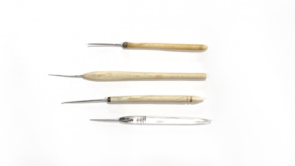 Tiny crochet needles made carved of marine ivory; bottom needle is made of reclaimed airplane glass. 